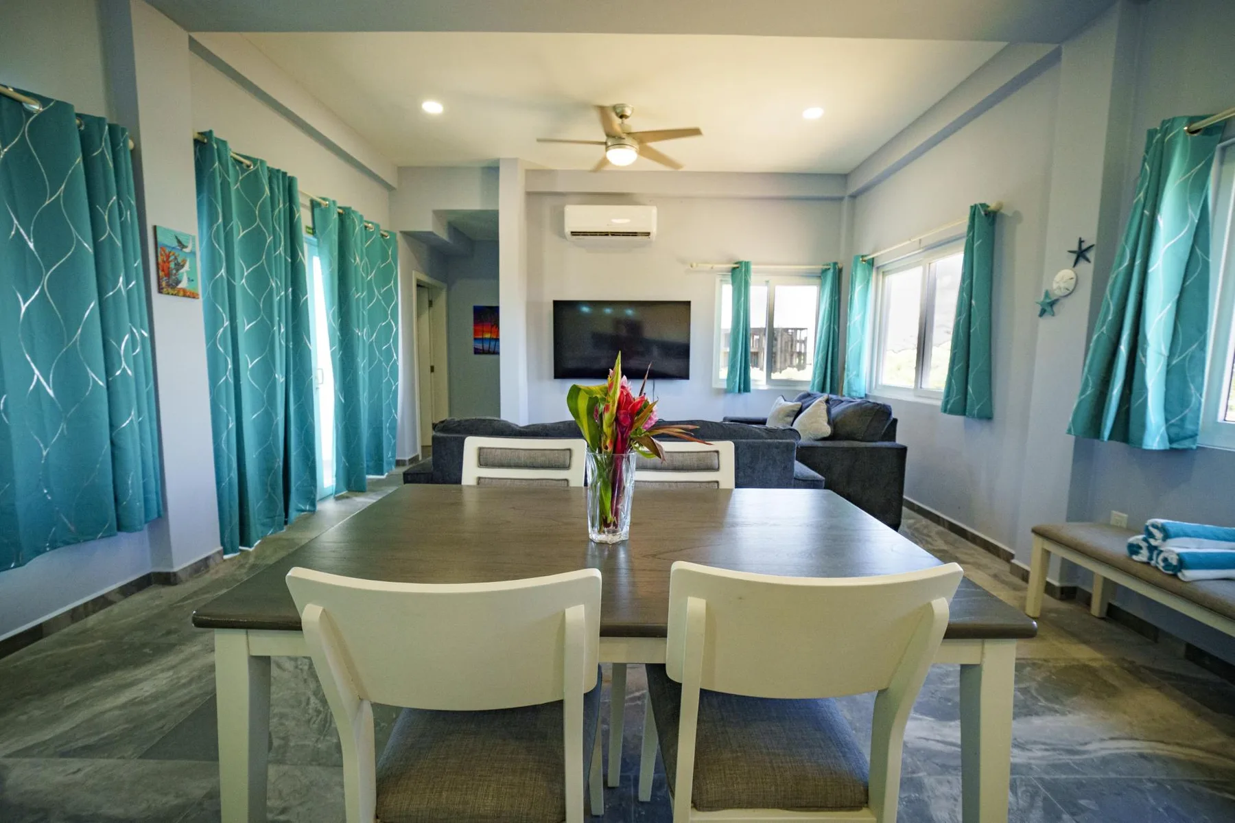 A dining table with flower centerpiece faces a living area with a television and seating.