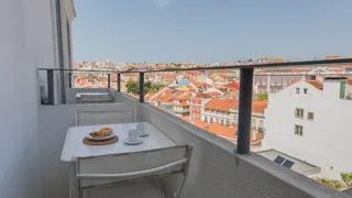 Una zona de comedor en un balcón da a un barrio de edificios con tejados rojos.