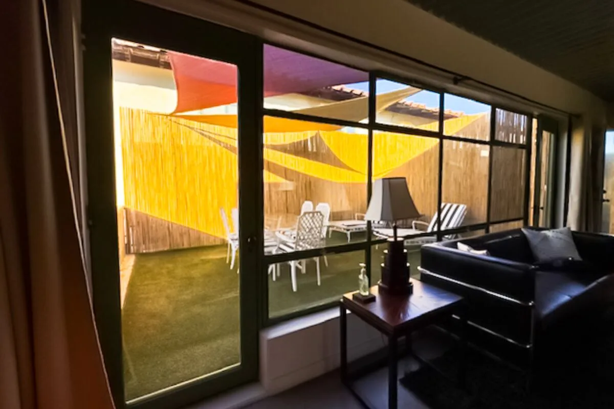 A living room opens onto a patio through large windows, with seating and a table.