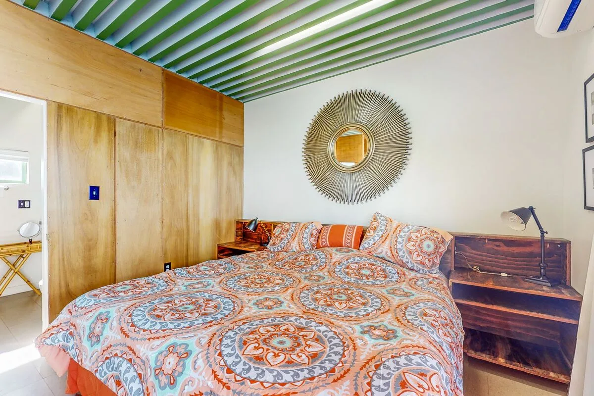 A bedroom with a large patterned bedspread and wooden storage along the wall.