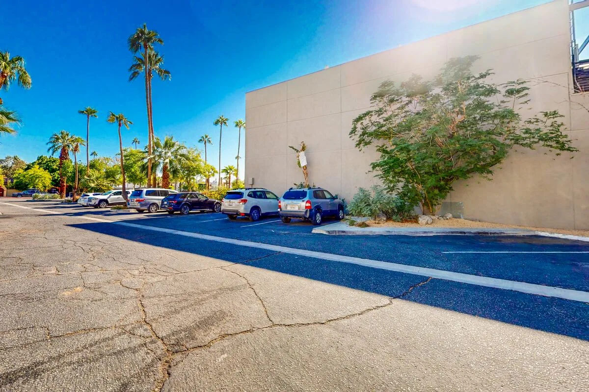 Shared amenity: Outdoor parking area with several cars beside a large wall and palm trees.