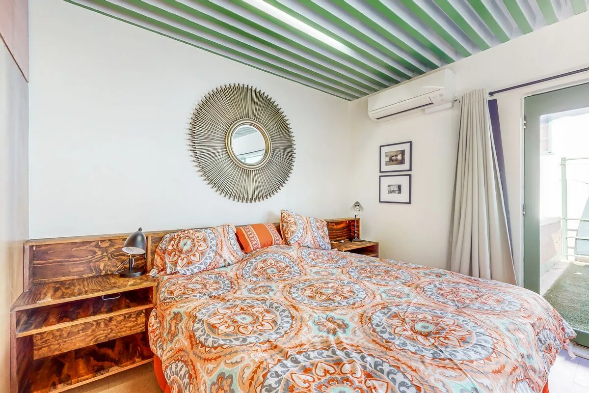 A bedroom with a patterned bedspread, wooden bedside tables, and a round wall mirror.
