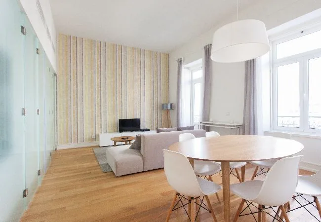 A bright living and dining area with a round table beside large windows.