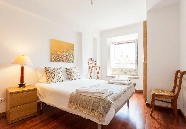 Un dormitorio luminoso con una cama, una mesita de noche y una ventana grande.