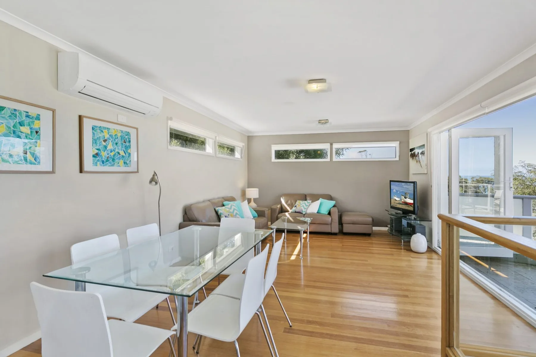 A bright living and dining area with seating, a glass dining table, and balcony windows.