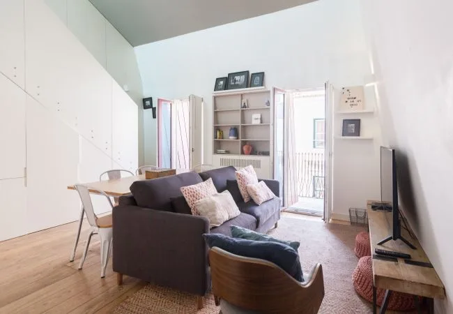 A bright living room with dark seating, a dining table, and a television.