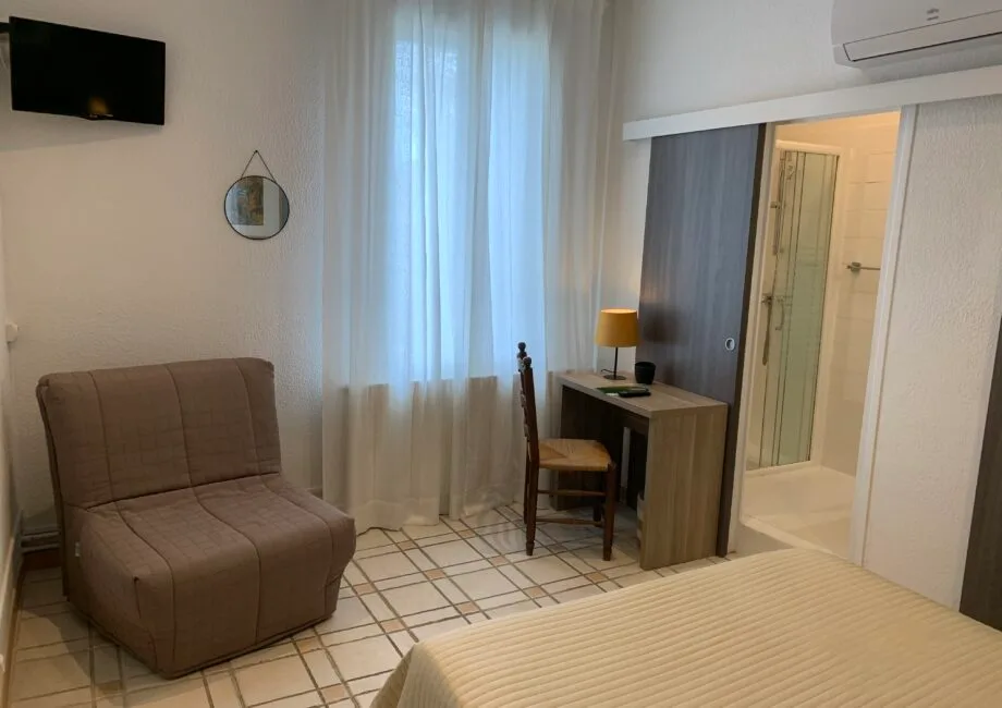 Representative hotel space: A bedroom with a bed, a desk, and an upholstered seat beside the window.
