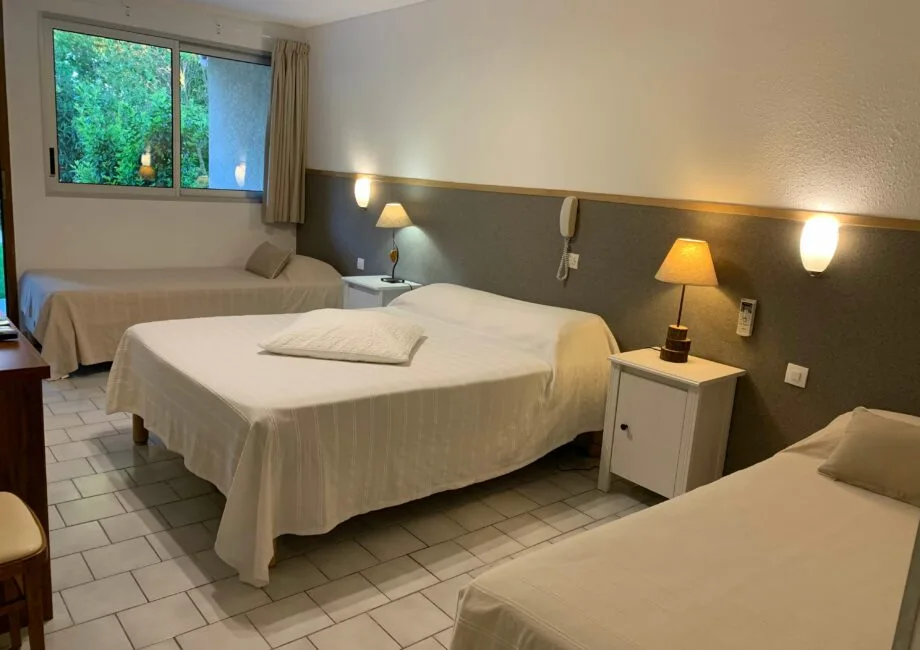Representative hotel space: A bedroom with several beds, bedside tables, and a window overlooking greenery.