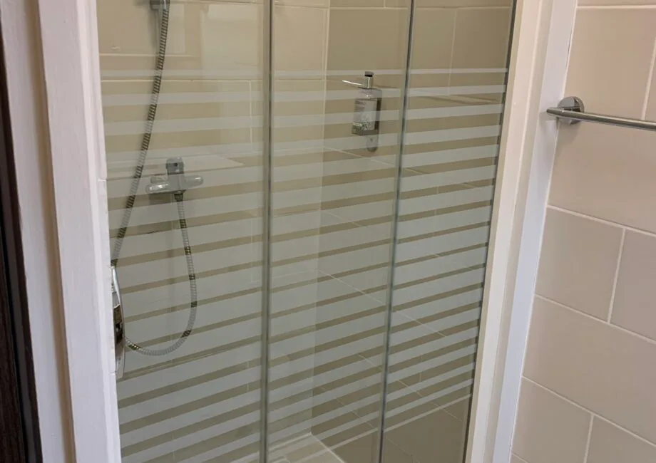 Representative hotel space: A tiled bathroom shower with glass panels and horizontal stripes.