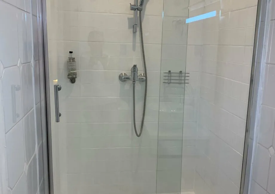 Representative hotel space: A tiled shower with a handheld showerhead and glass panels.