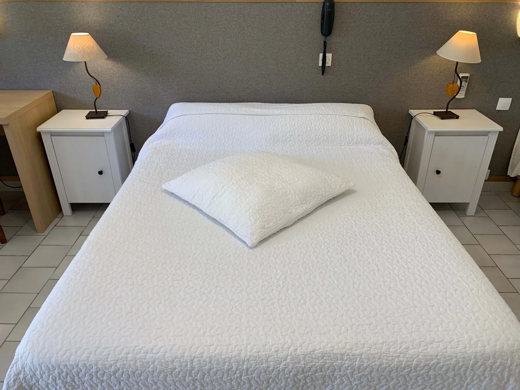 Representative hotel space: A neatly made bed sits between two bedside tables with lamps.