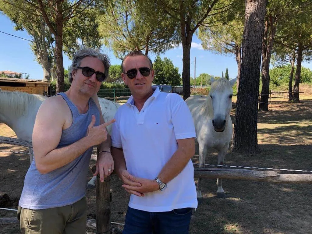 Representative hotel space: Two men pose beside a white horse in a shaded outdoor paddock.