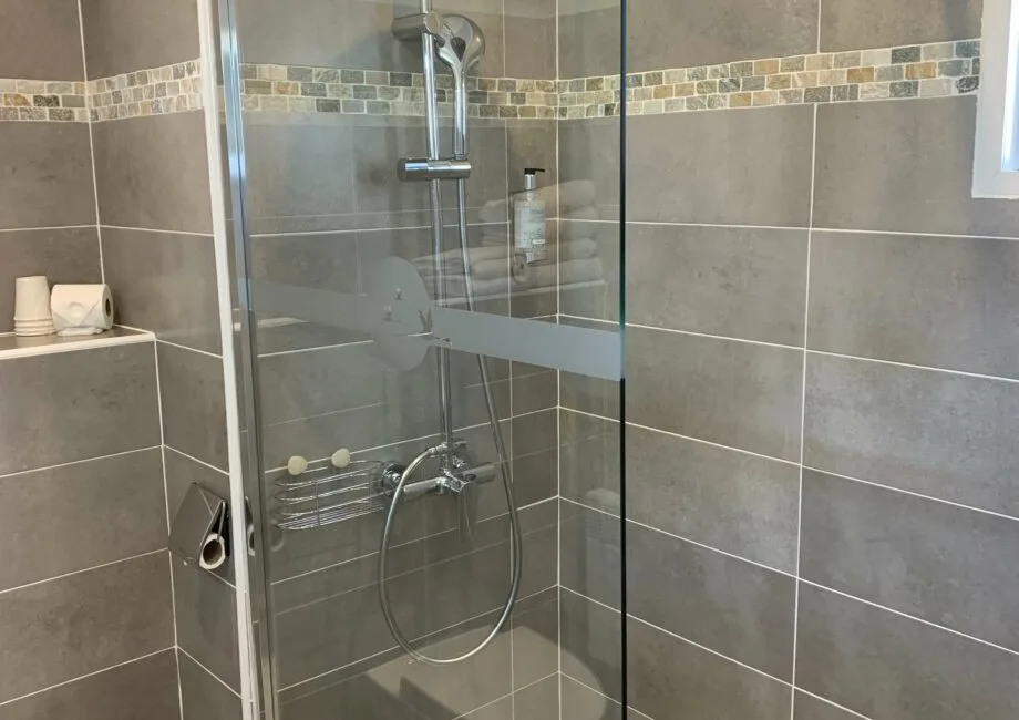 Representative hotel space: A tiled bathroom shower with glass panels and a handheld showerhead.