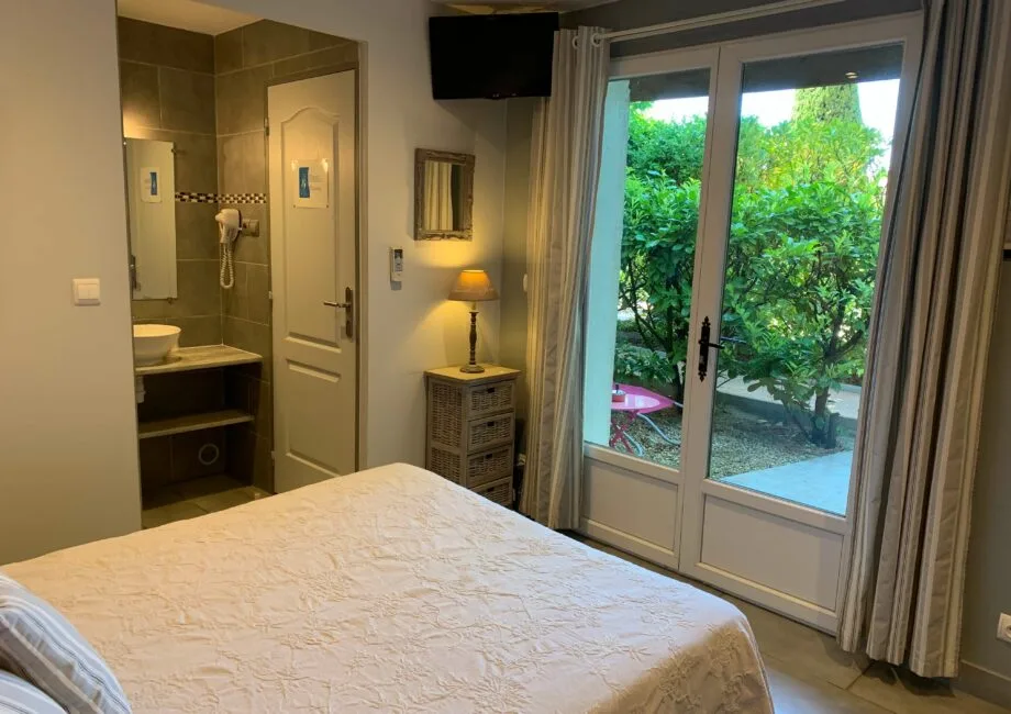 Representative hotel space: A bedroom with a bed, a compact bathroom area, and glass doors opening to greenery.