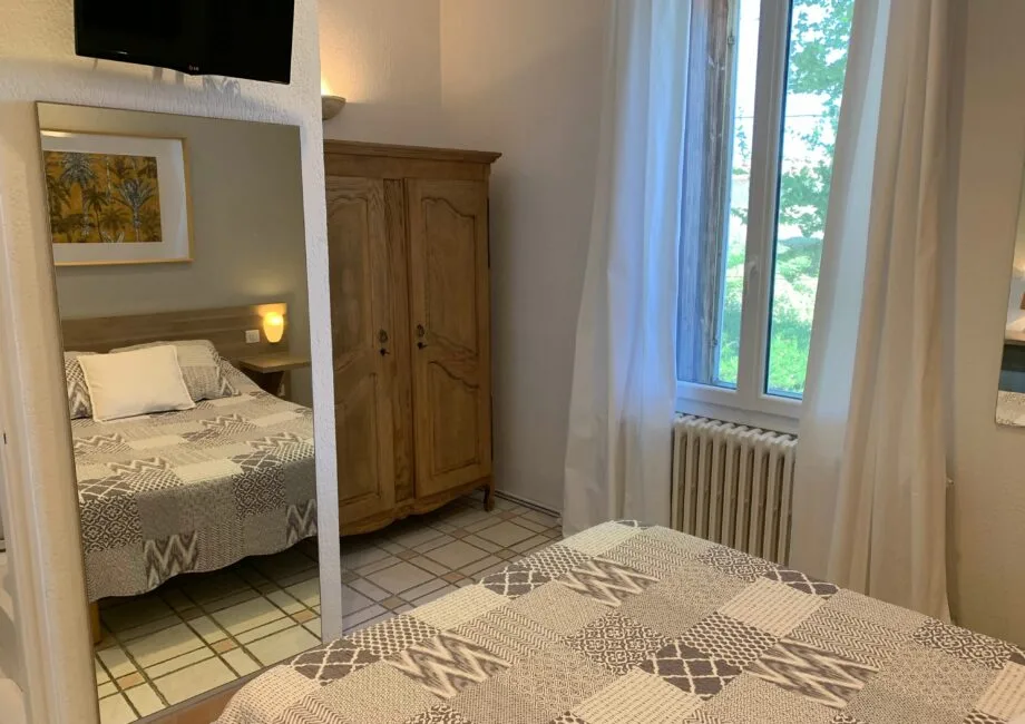 Representative hotel space: A bedroom with patterned bedding, a wooden wardrobe, and a tall window.
