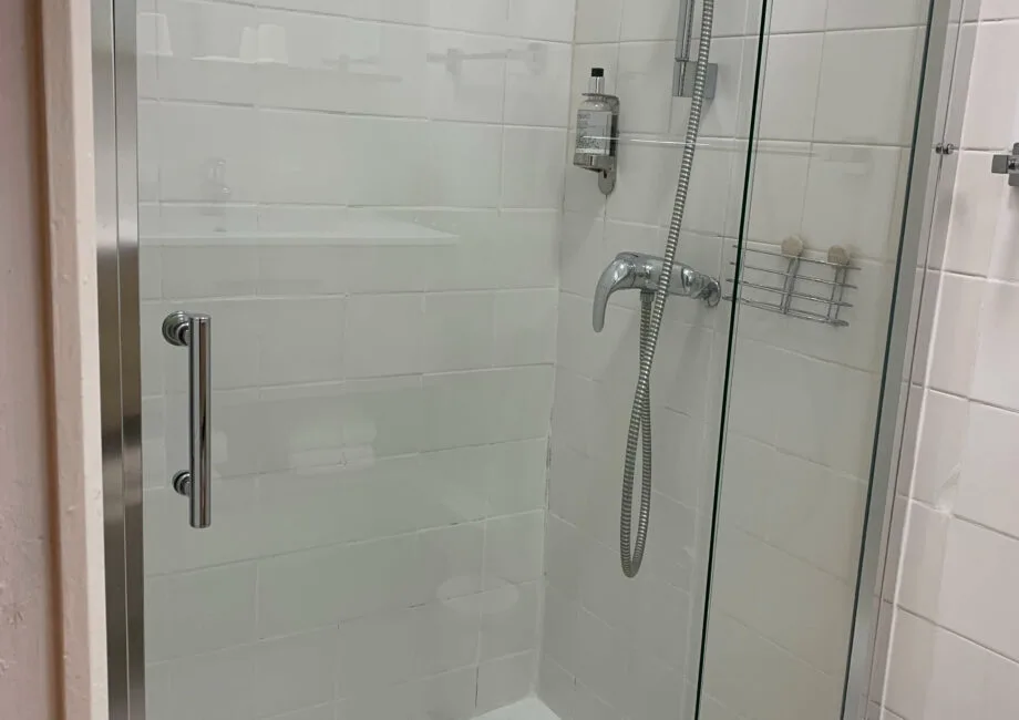 Representative hotel space: A tiled bathroom shower with a glass door and handheld showerhead.