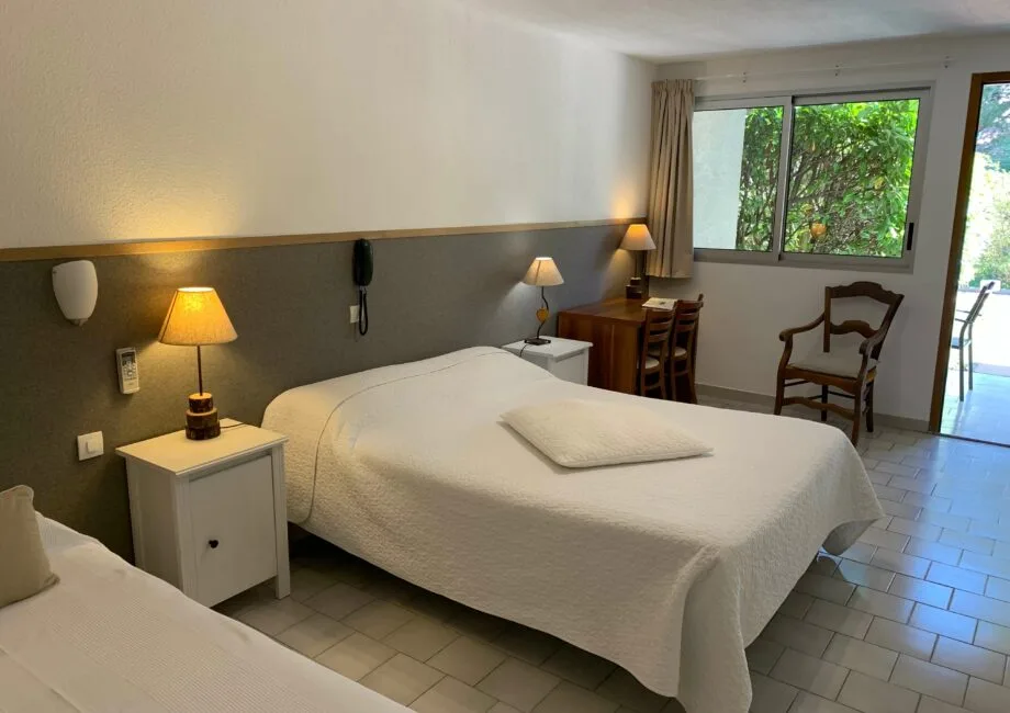 Representative hotel space: A bedroom with two beds, bedside lamps, and a window overlooking greenery.
