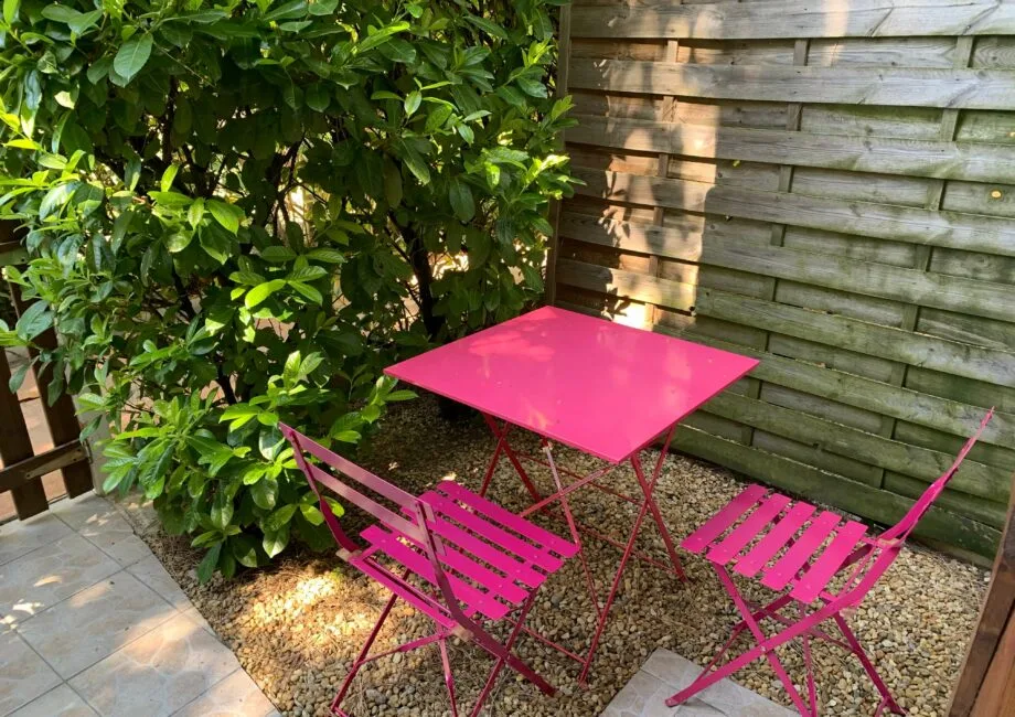 Representative hotel space: A small outdoor patio with bright pink seating beside leafy shrubs and a wooden fence.