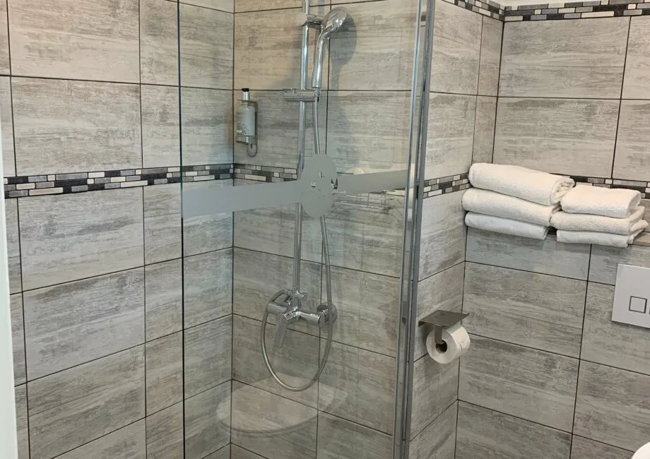 Representative hotel space: A tiled bathroom with a glass shower and folded towels on a shelf.