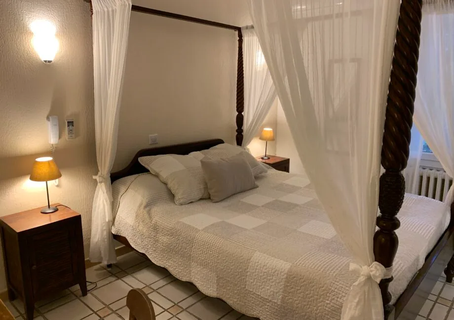Representative hotel space: A bedroom with a bed framed by white curtains and dark wooden posts.