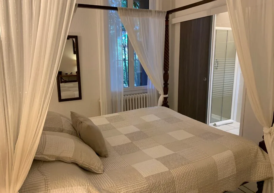 Representative hotel space: A bedroom with a bed beneath sheer curtains and a window behind it.