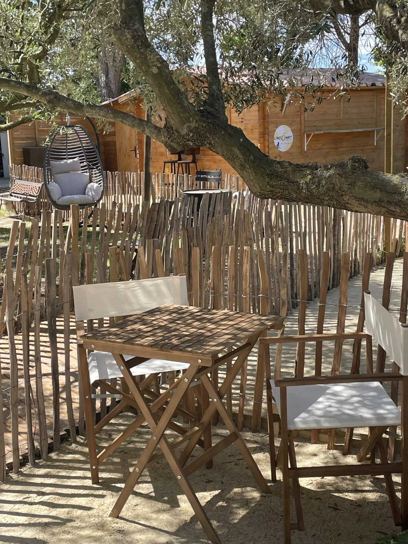 Representative hotel space: An outdoor seating area with wooden tables and chairs beneath leafy trees.