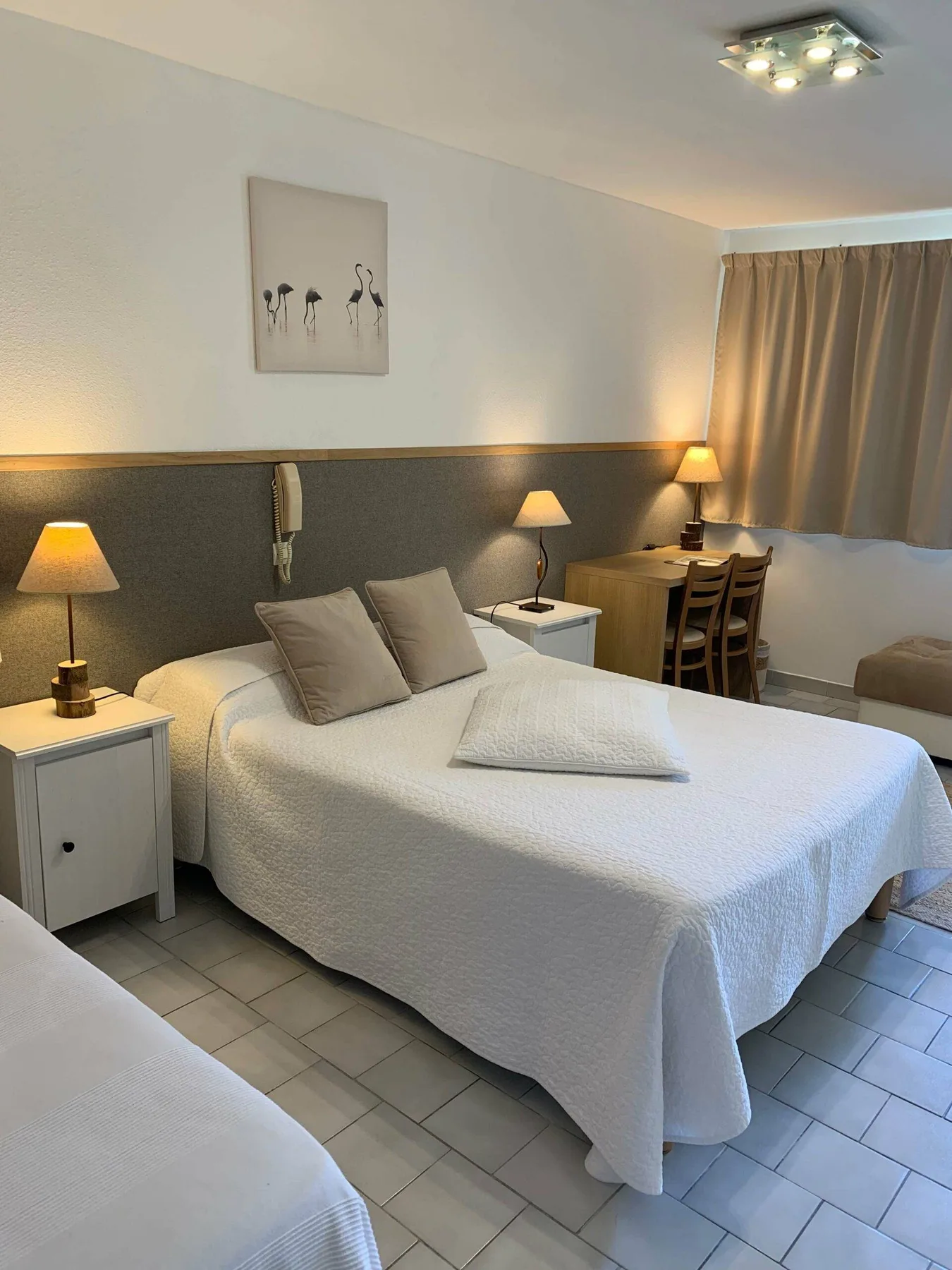 Representative hotel space: A bedroom with a white bed, bedside tables, and a desk by the window.