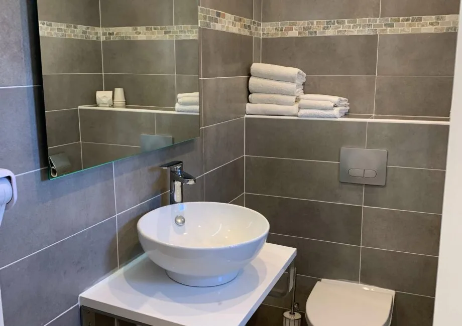 Representative hotel space: A tiled bathroom with a vessel sink and folded towels on a wall shelf.