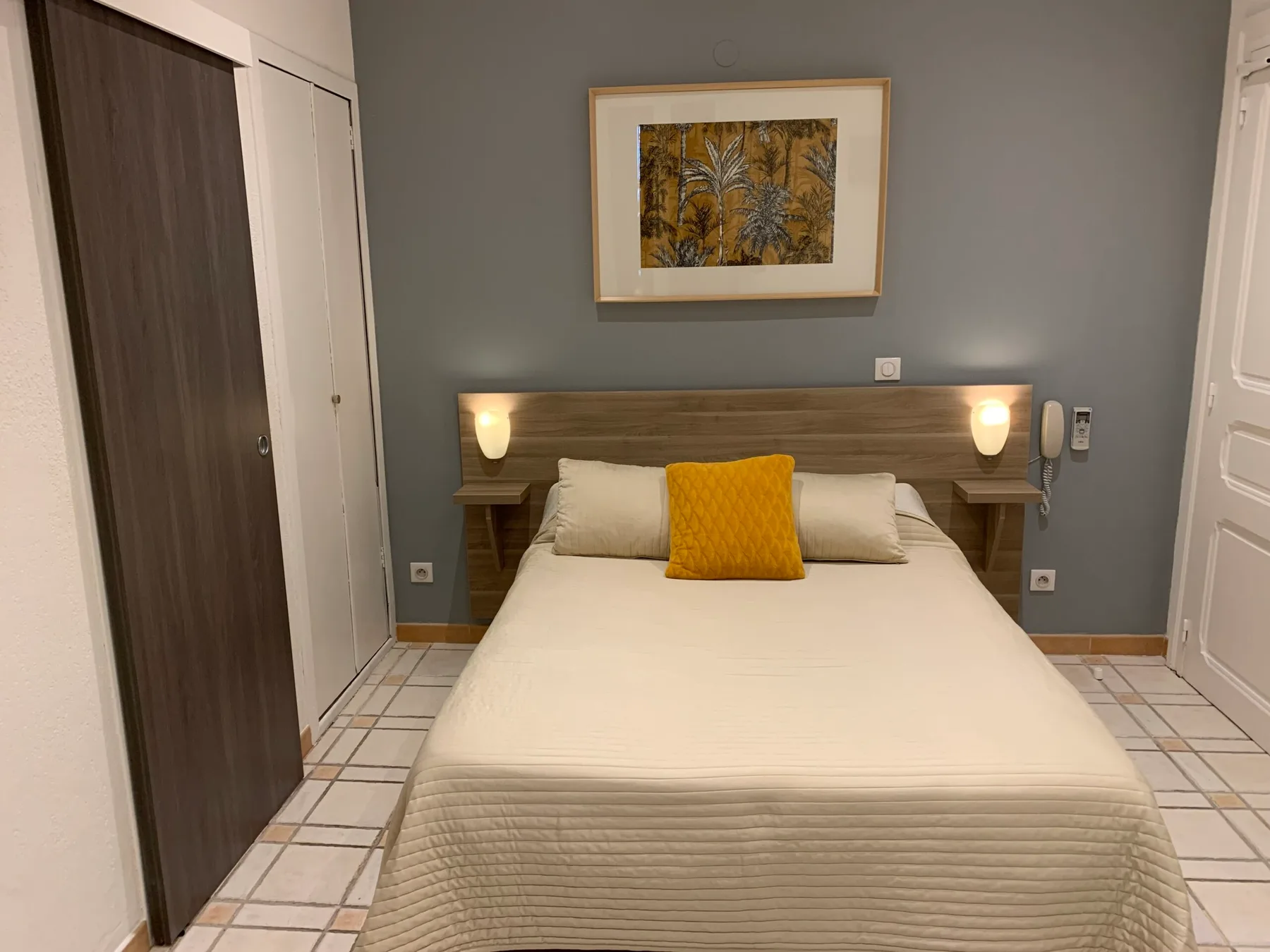 Representative hotel space: Bedroom with a neatly made bed, mustard-colored accent pillow, and framed artwork.