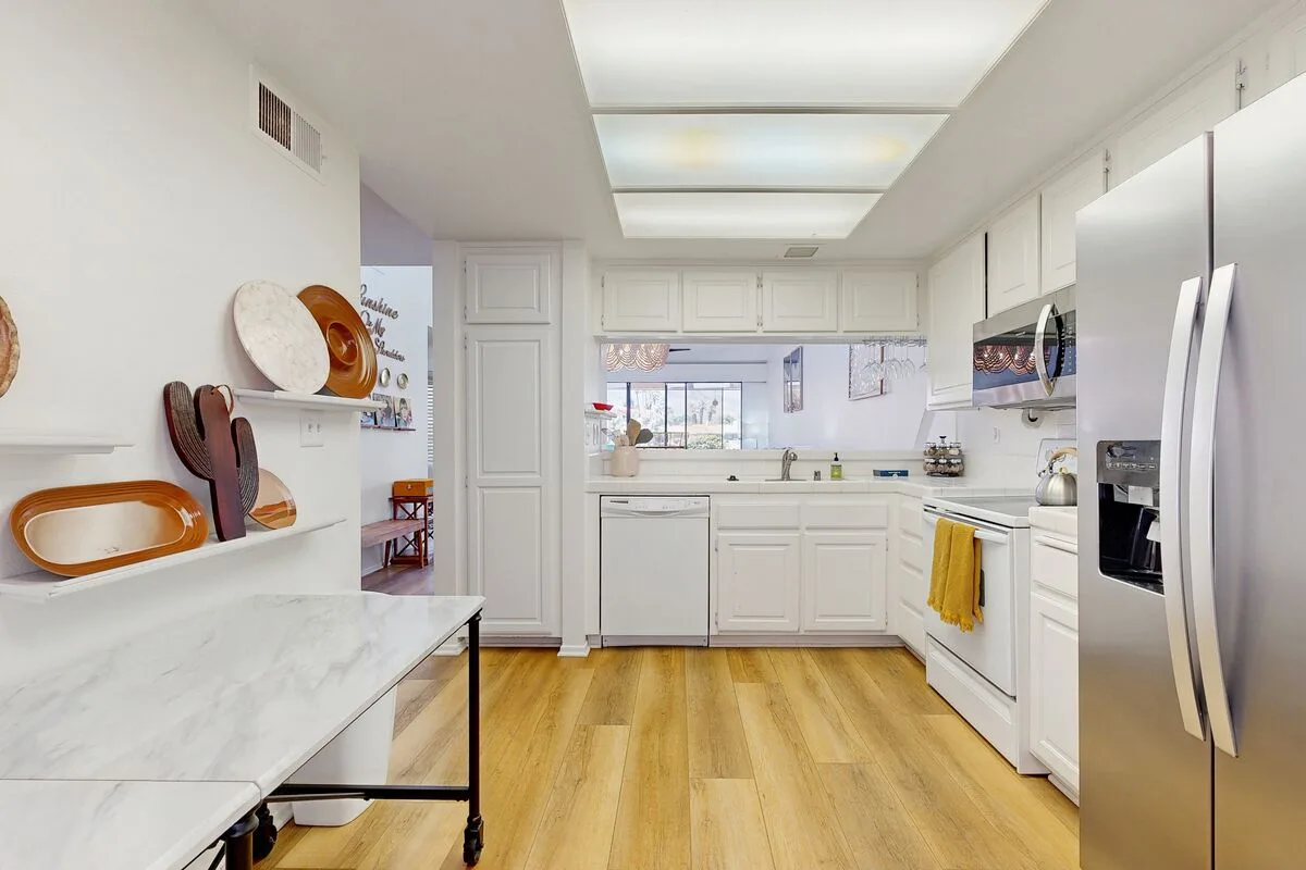 A bright white kitchen with a central sink and stainless steel appliances.