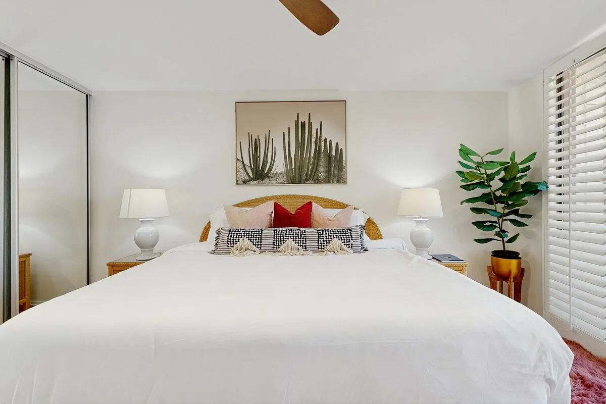 A bright bedroom with a neatly made bed, matching bedside lamps, and framed cactus art.
