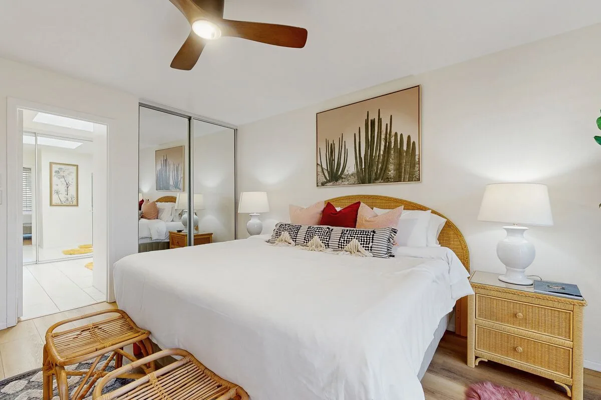 A bright bedroom with a white bed, bedside tables, and framed cactus artwork.