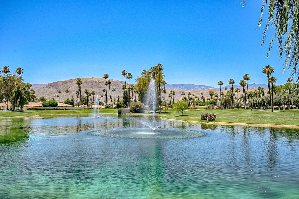 Shared amenity: A landscaped pond with fountains sits among palm trees beneath a clear sky.