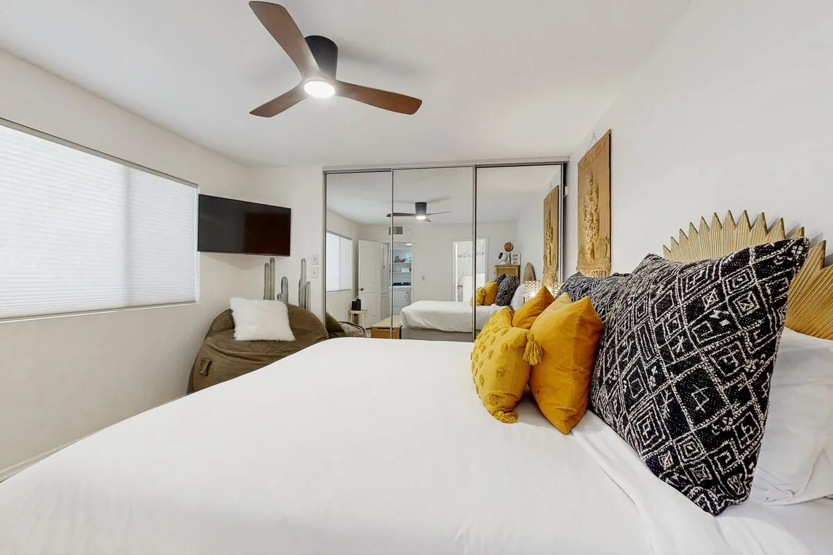 A bright bedroom with a bed dressed in white and patterned pillows.