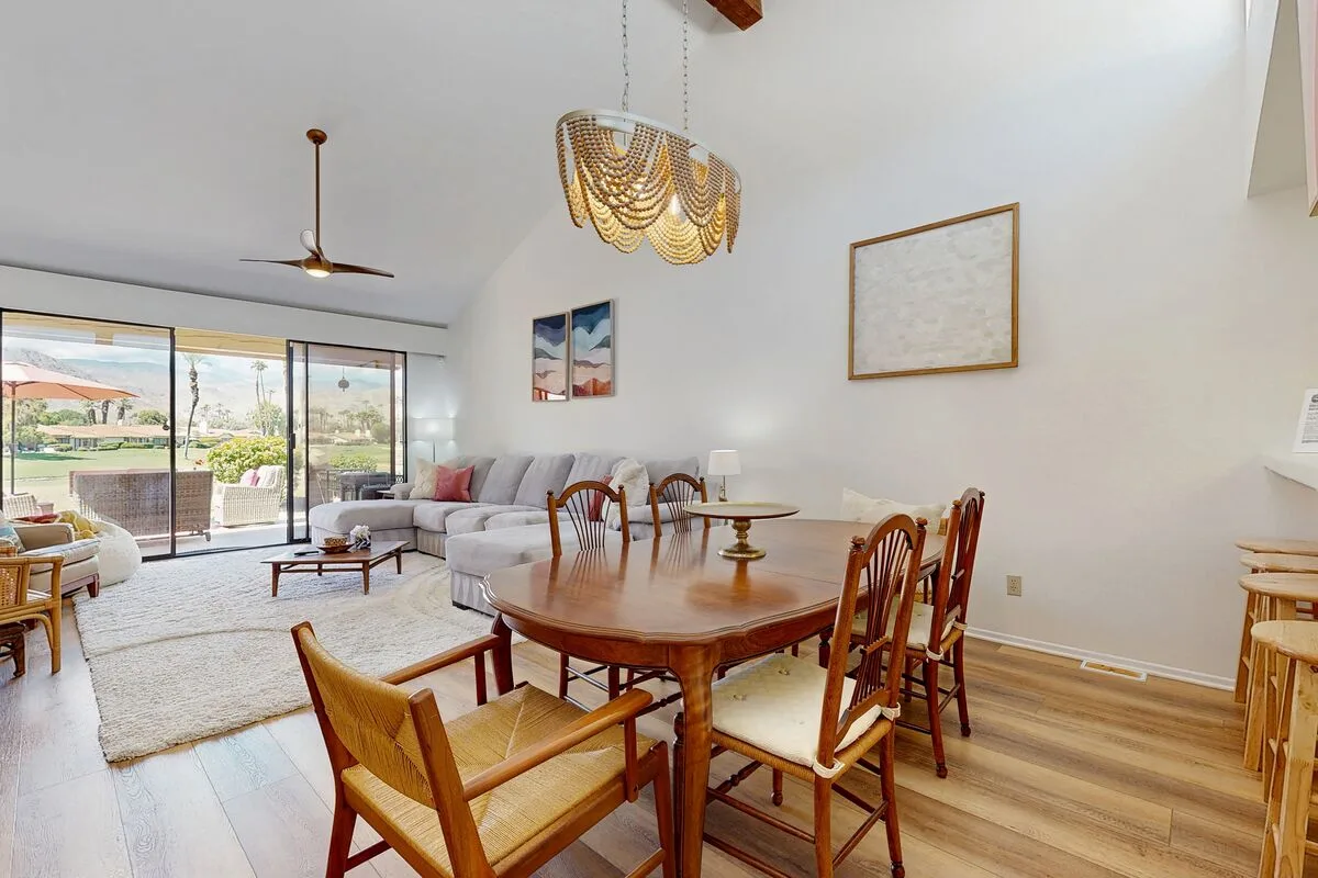 A dining area with wooden seating beside a bright living room and sliding glass doors.