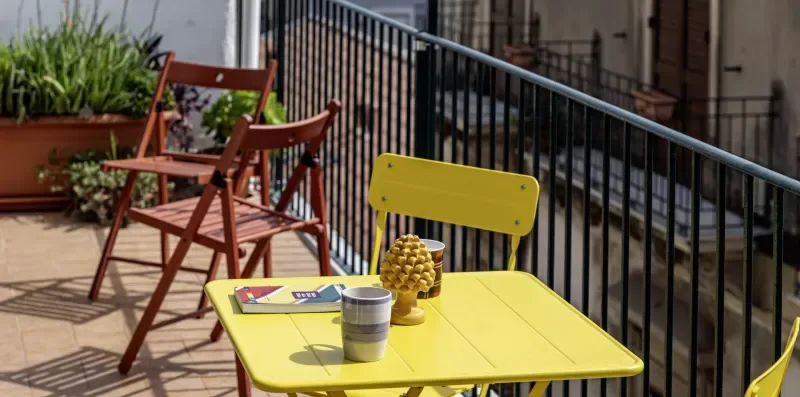 Una pequeña zona de estar al aire libre con una mesa amarilla junto a una barandilla.