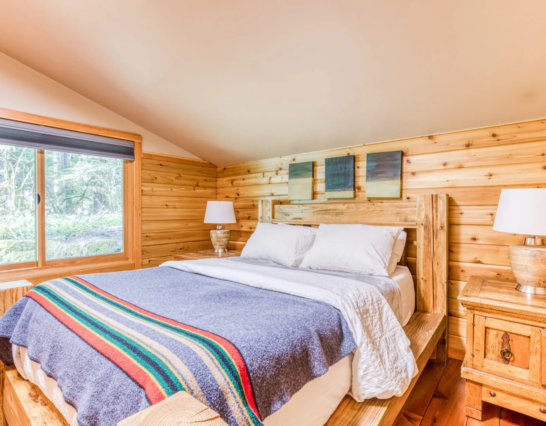 Un dormitorio con una cama, lámparas de noche y una ventana grande.