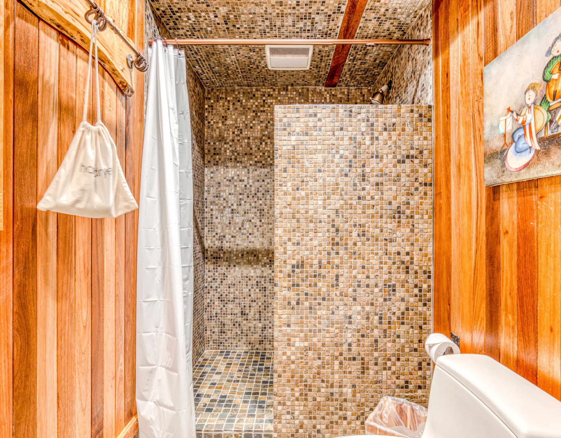 Un baño alicatado con ducha, cortina blanca y paredes revestidas de madera.
