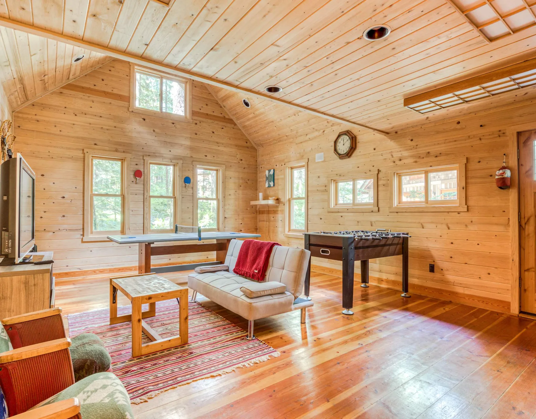 Una sala de juegos revestida de madera, con mesa de billar, asientos y ventanas amplias.