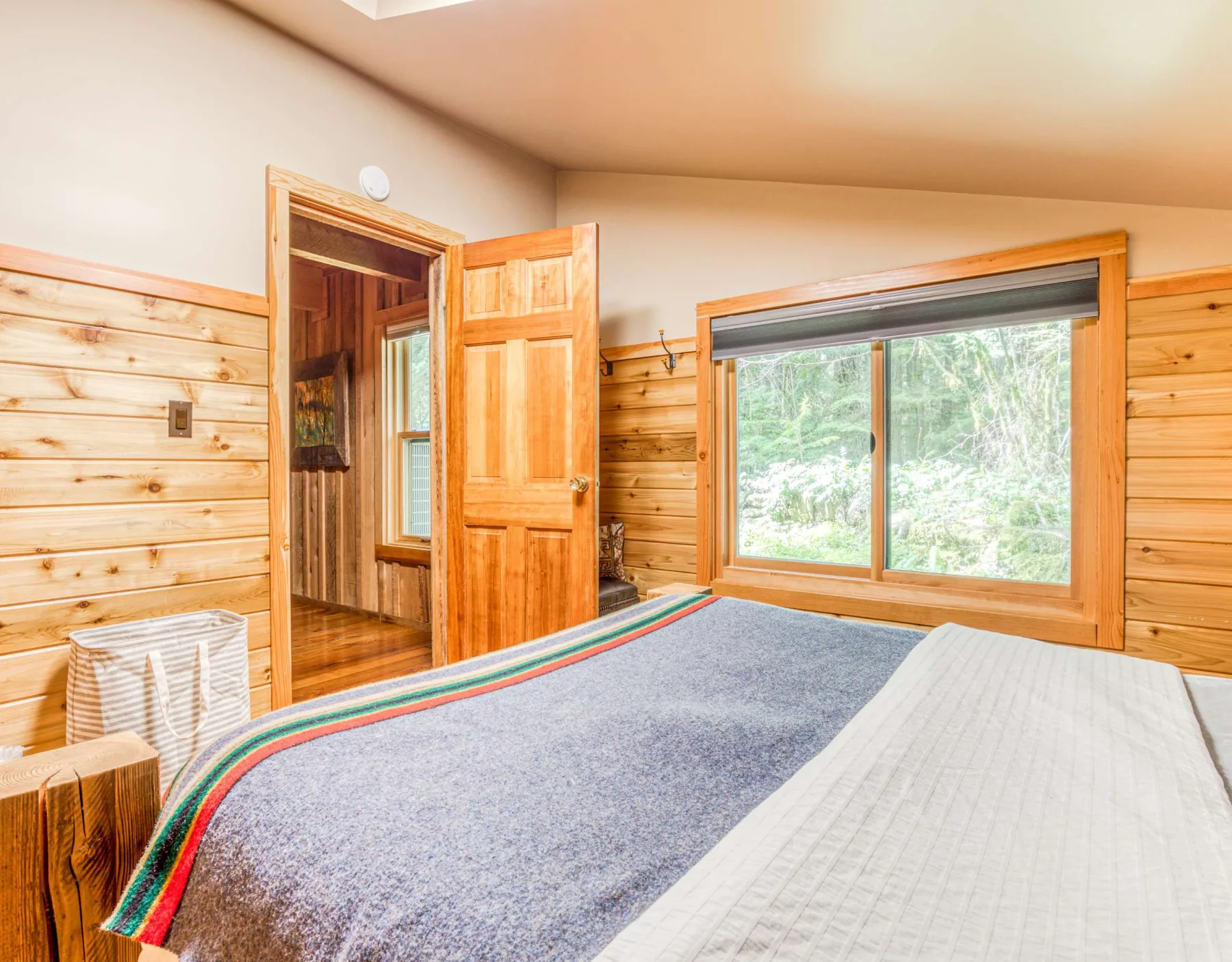 Un dormitorio con una cama, paredes revestidas de madera y una ventana grande.