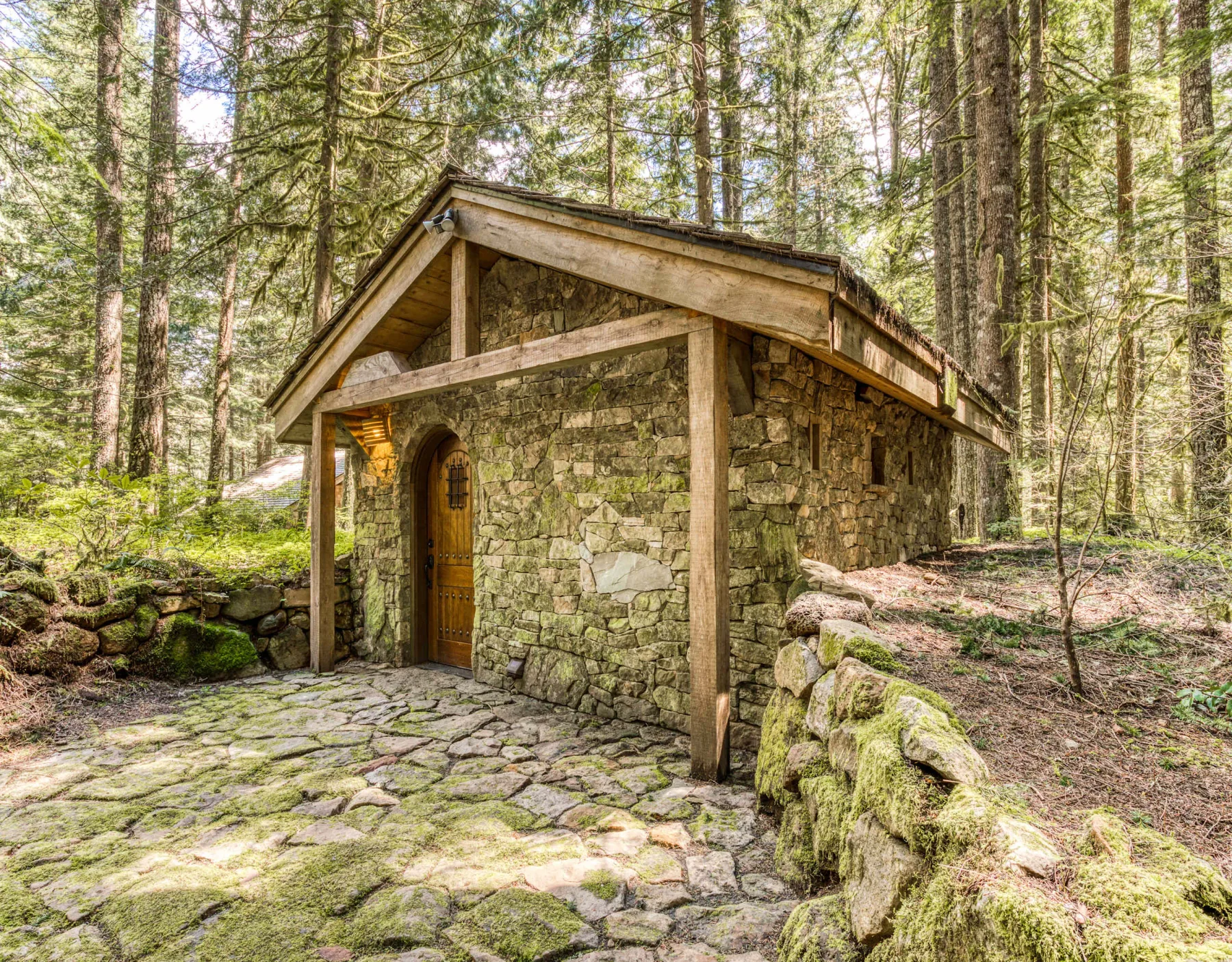 Un pequeño edificio de piedra con techo de madera está entre árboles.