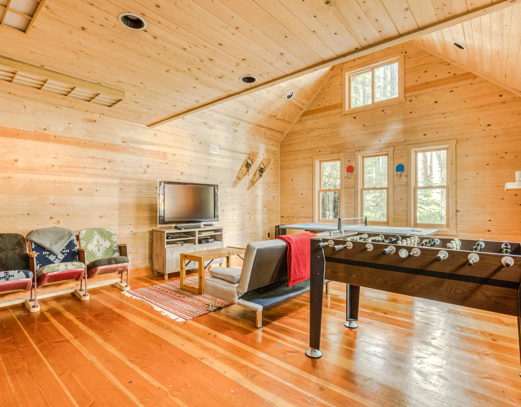 Sala de recreación revestida de madera con futbolín, asientos y televisor.
