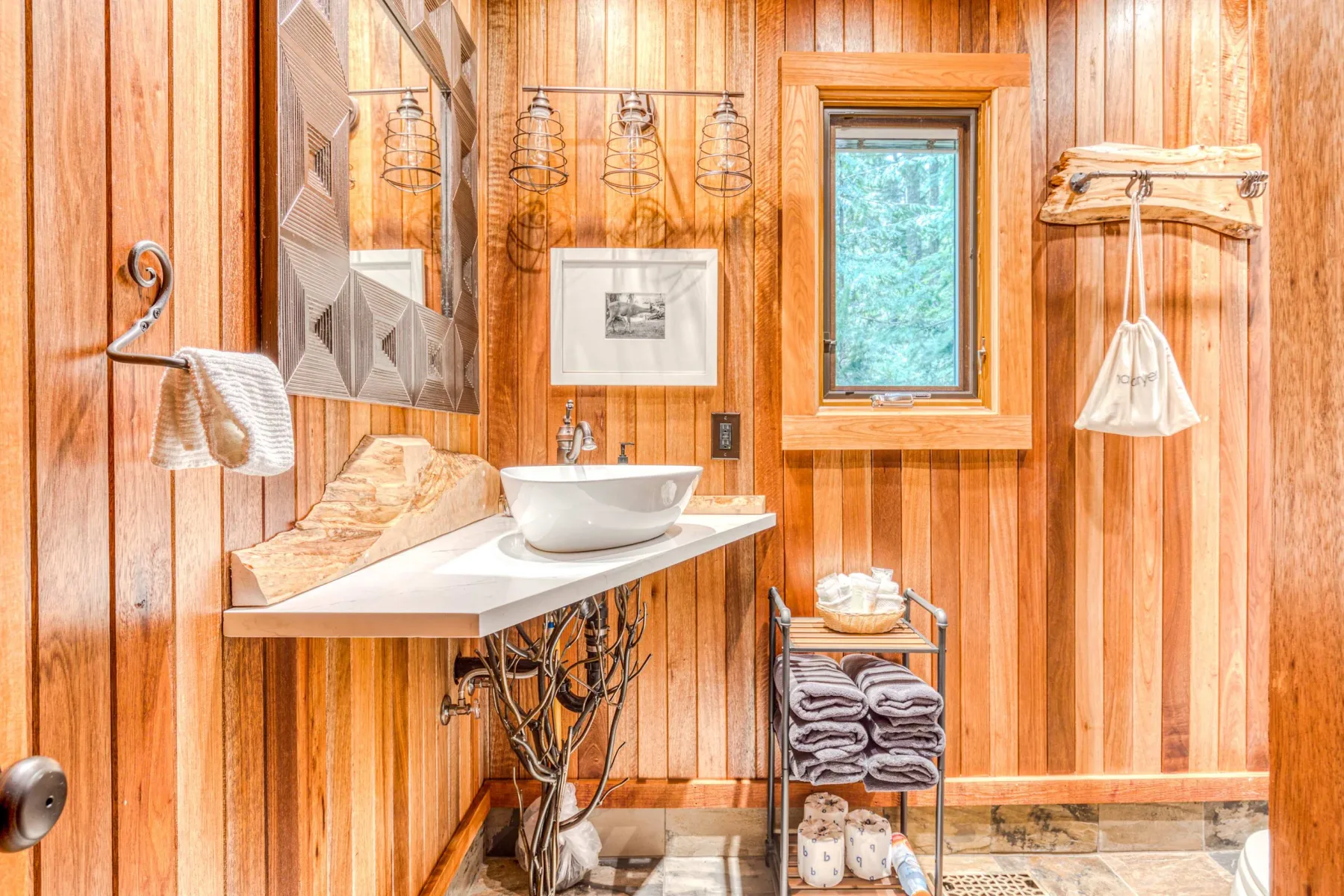 Un baño revestido de madera con lavabo, espejo y ventana.