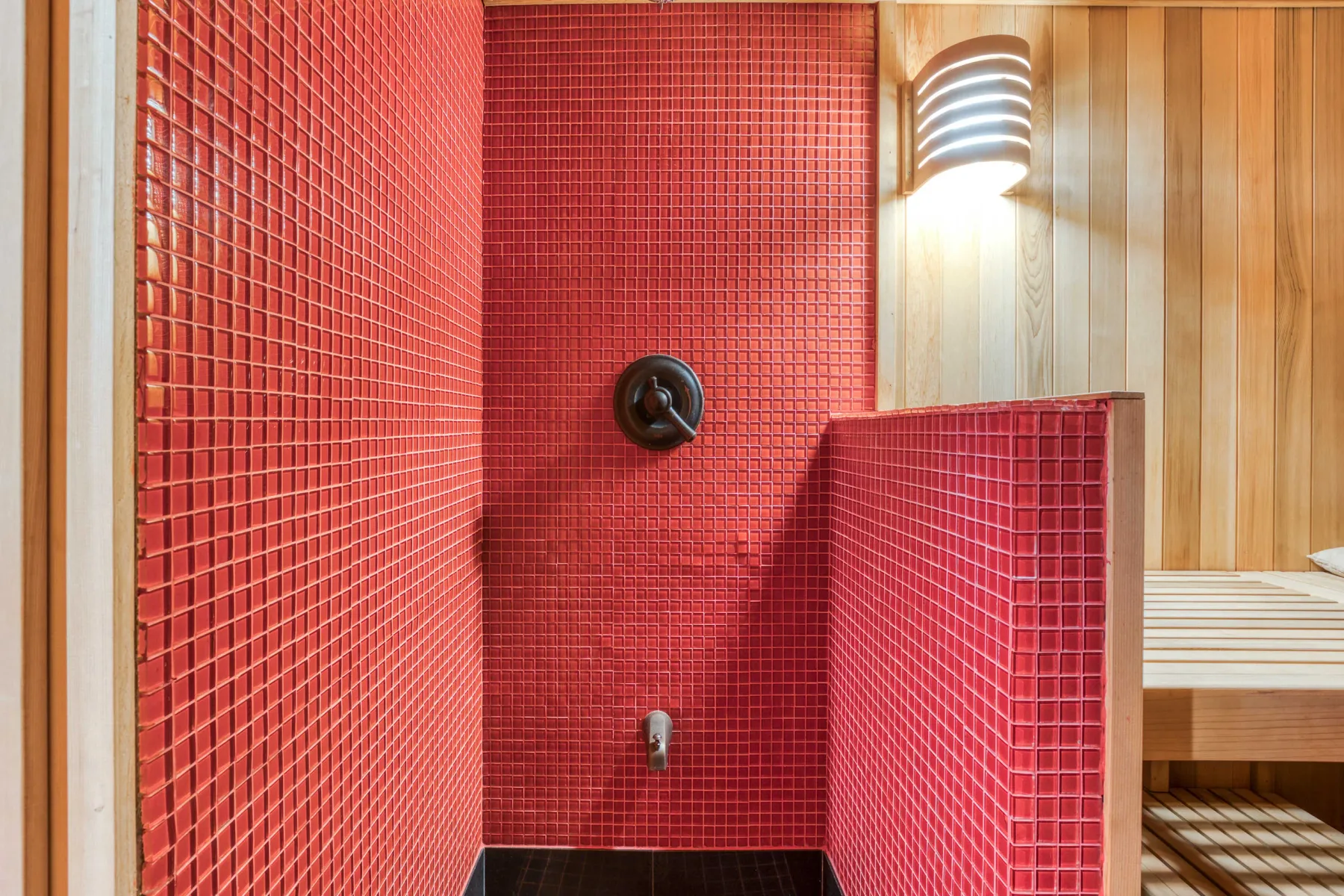 Una zona de ducha con azulejos rojos junto a una pared de sauna revestida de madera.