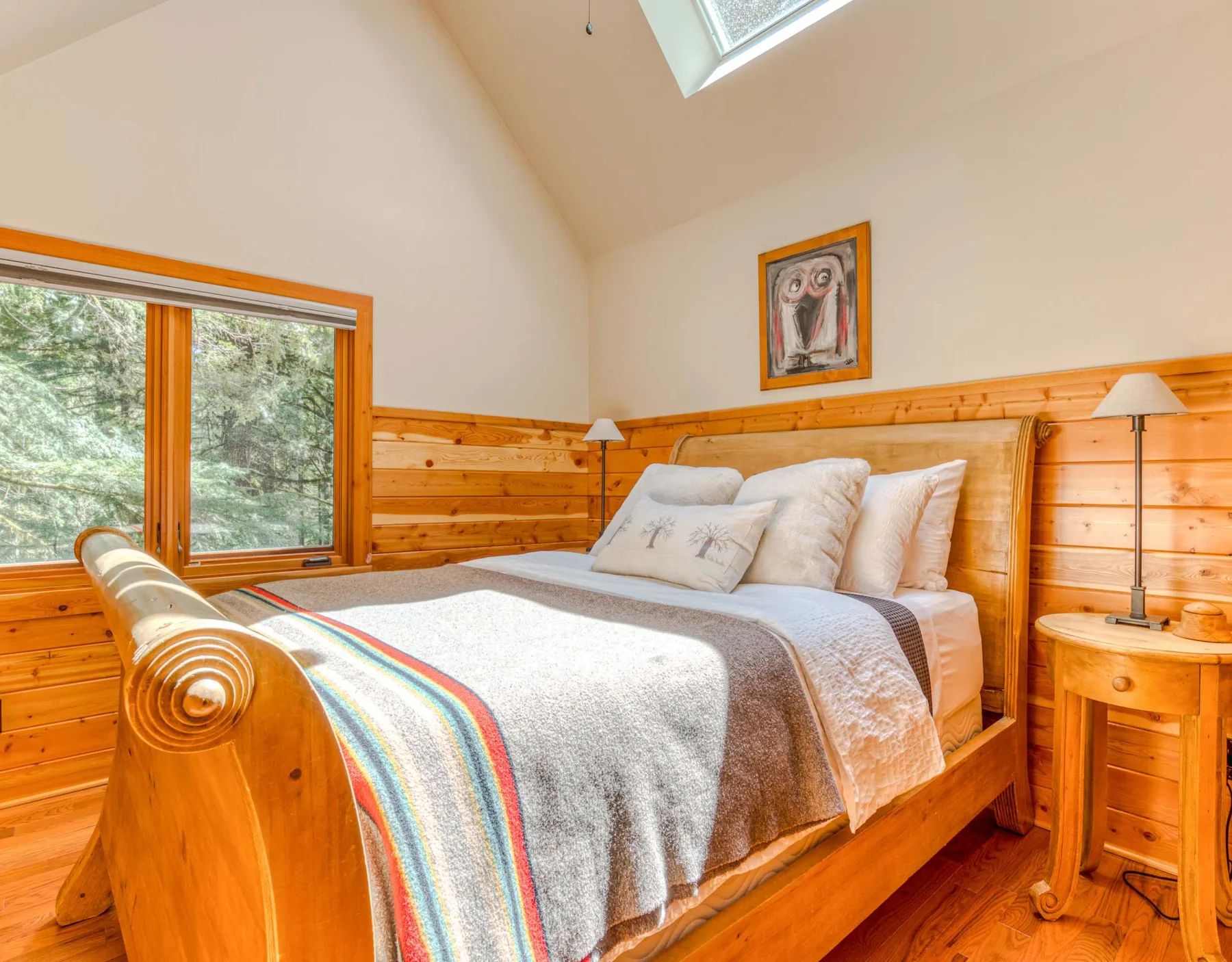 Un dormitorio revestido de madera con una cama, mesitas de noche y una ventana grande.
