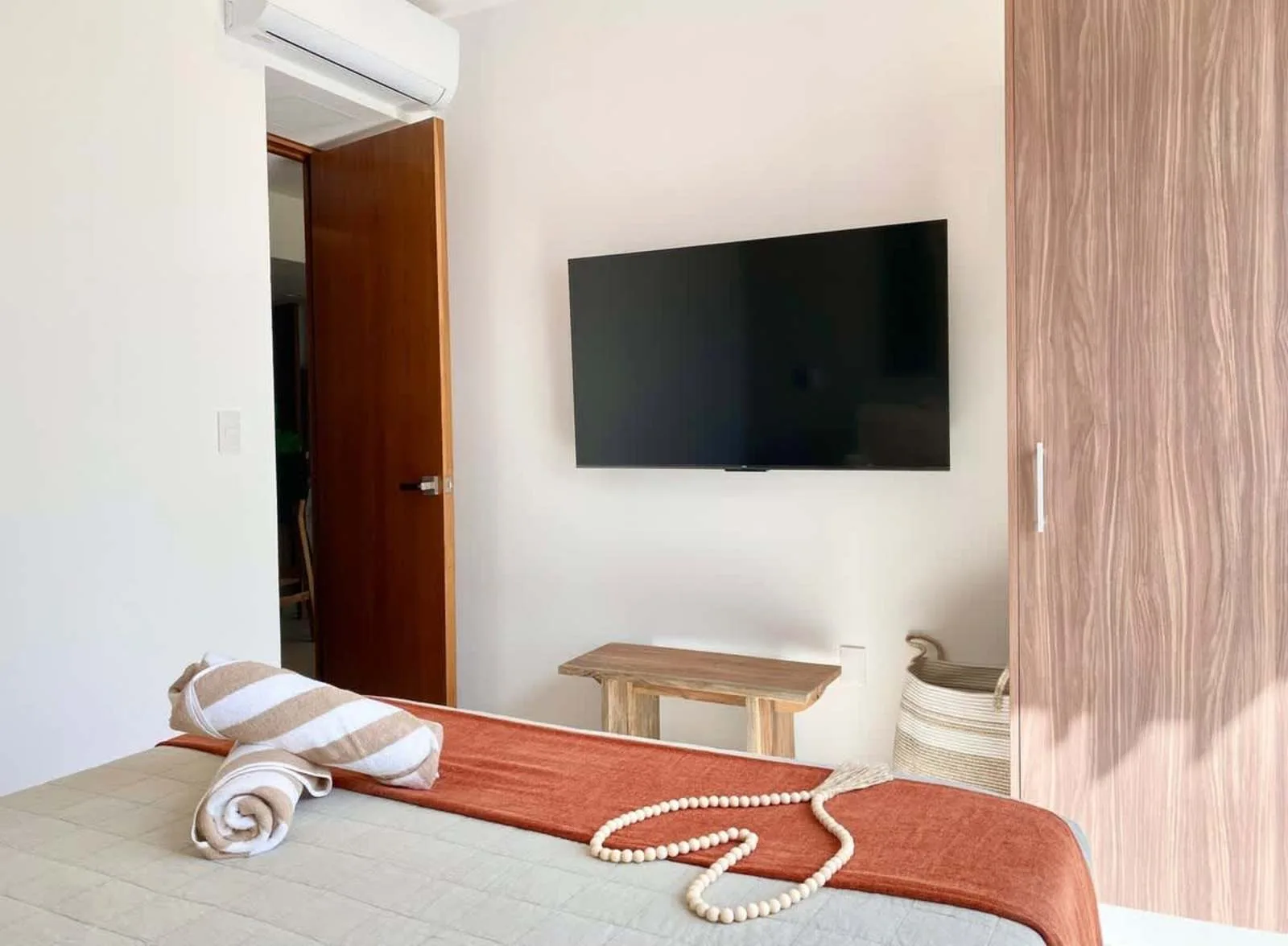 Un dormitorio con una cama, un televisor en la pared y una puerta de madera abierta.