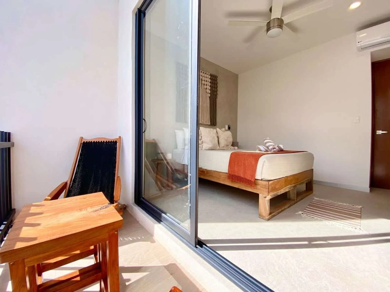 Un dormitorio con cama, ventilador de techo y puerta corrediza de vidrio que da a un pequeño patio.