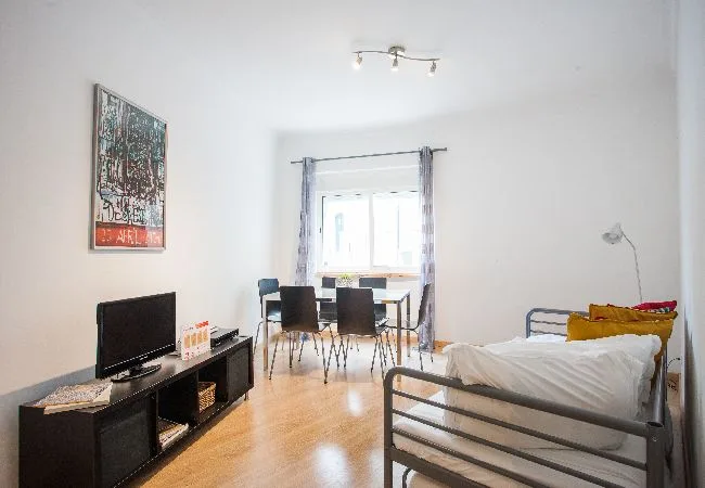 A bedroom with a bed, a television, and a small dining area by the window.