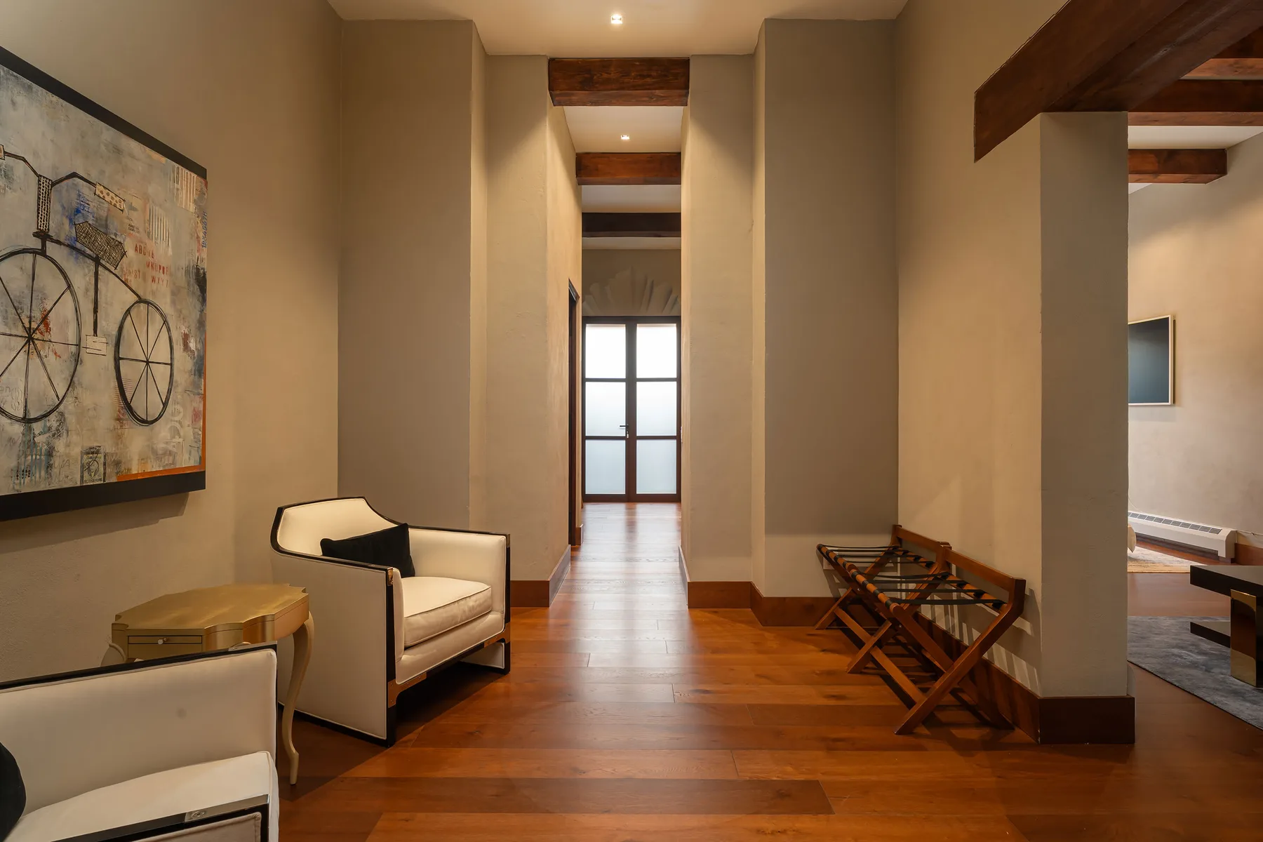 A warm-toned hallway with seating, a framed artwork, and a table by the far window.