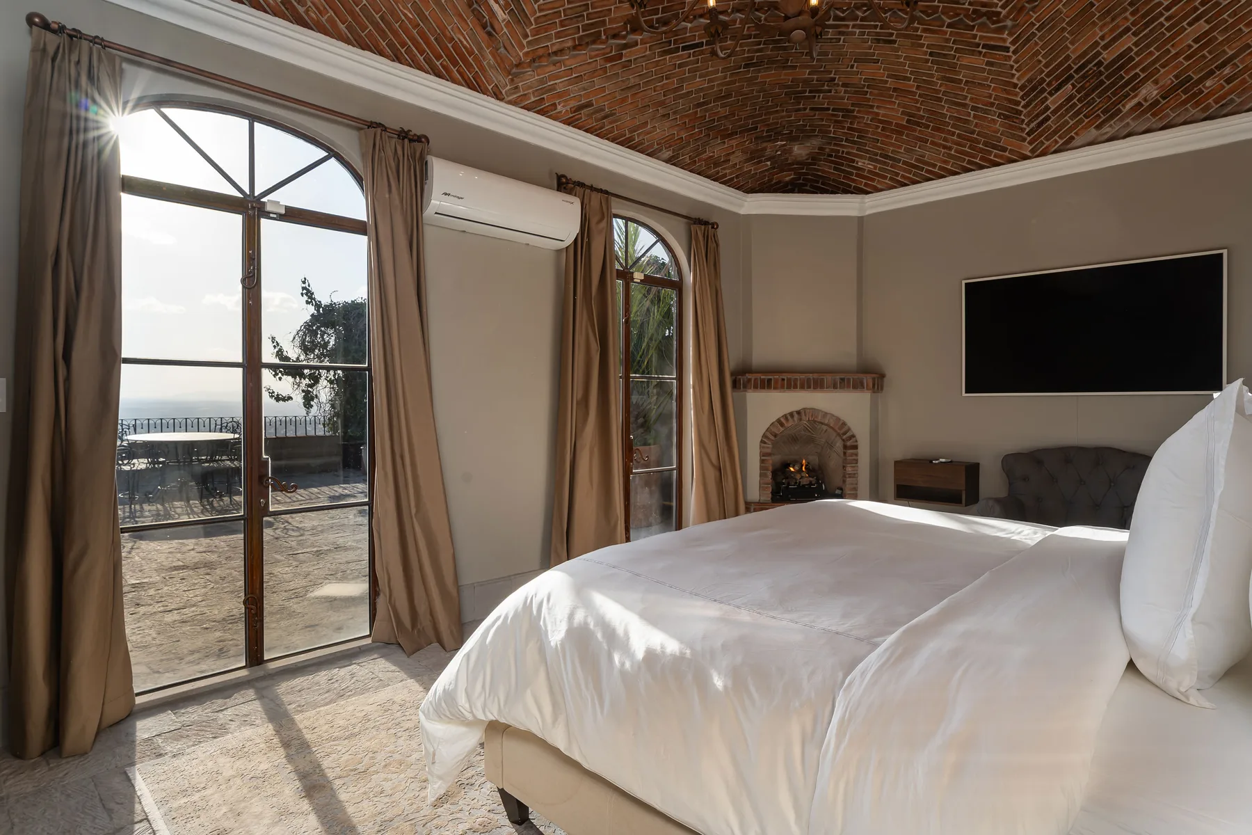A bedroom with a large bed, arched windows, and a brick ceiling.
